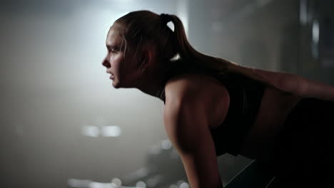 una mujer fuerte hace esfuerzos y superando dificultades levanta una mancuerna en un gimnasio oscuro. mujer de fitness levantando pesas entrenando mancuernas en el club de gimnasio.