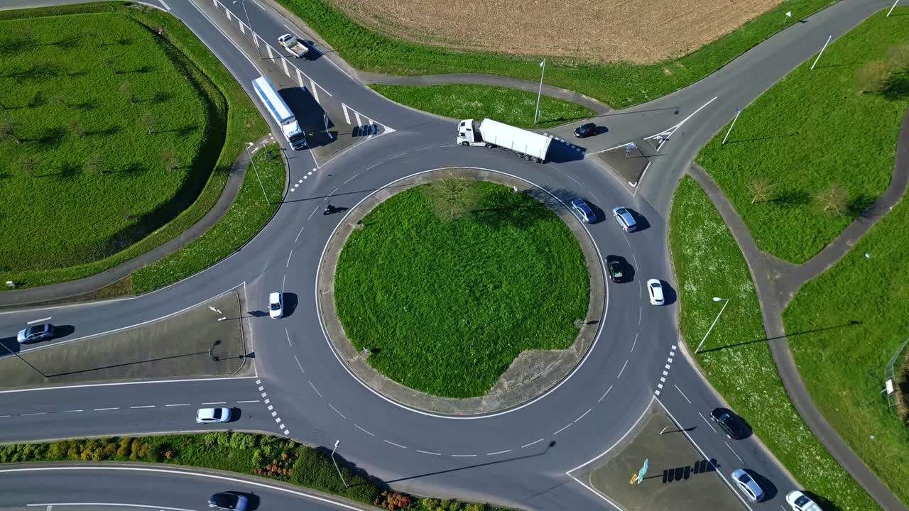 Cars and trucks driving on roundabout with green grass center, Infrastructure, transportation, road network. Aerial drone top-down view