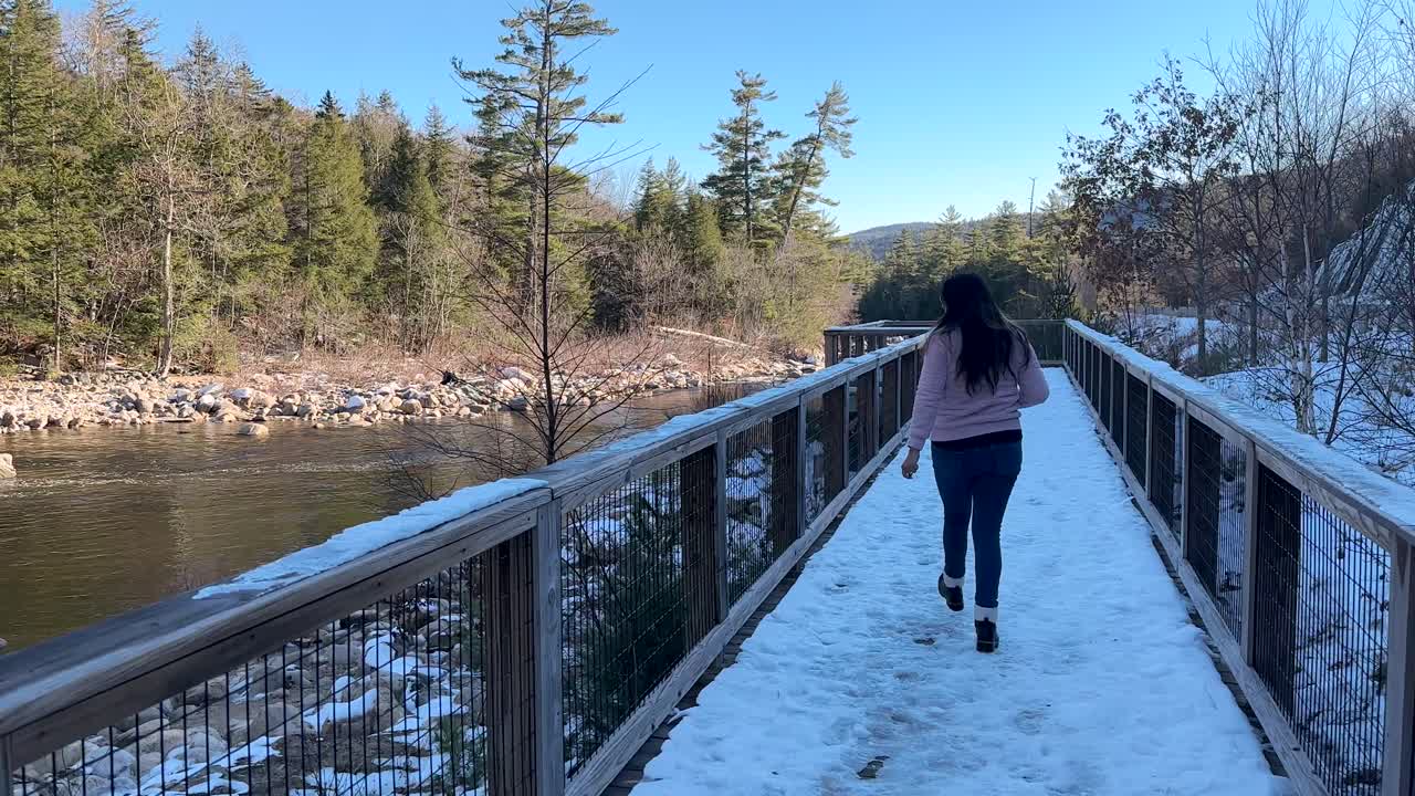 mujer despertando a través de un puente cubierto de nieve sobre un río en un bosque de invierno en un día claro