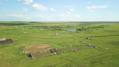 vast green fields near pond and houses - aerial drone shot