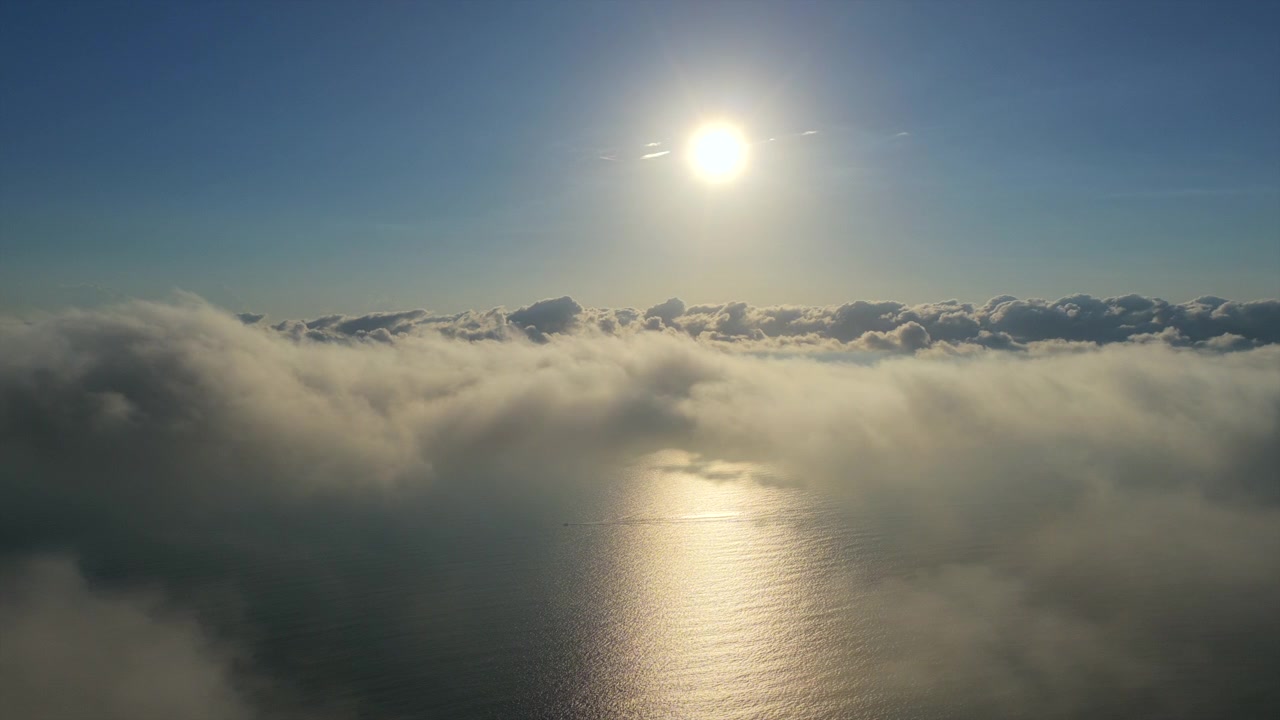 雲の層の上で太陽が明るく輝き、下の海面に反射している。自然の美しさや大気の状態を強調するプロジェクトに最適