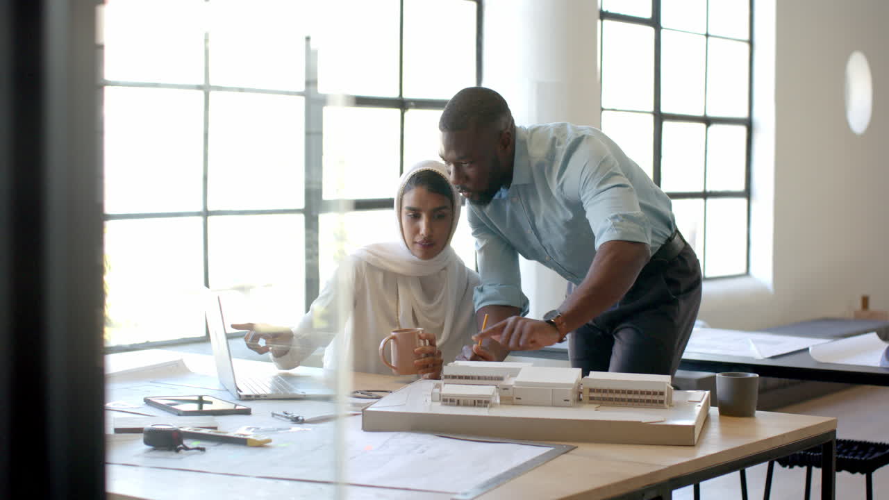 Collaborating on architectural project, colleagues using laptop and model in office