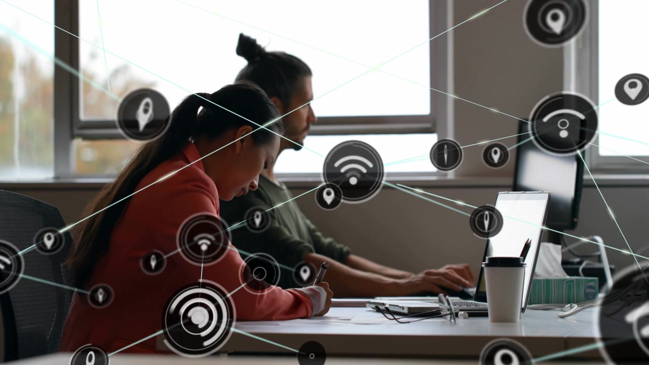 Woman writing and man typing at desk, laptop emitting network icons visualizing technology links
