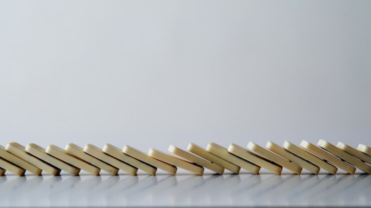 Domino pieces collapsing cascade on white surface closeup. Toy bricks falling