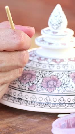 artist carefully painting traditional thai bowl at outdoor workshop