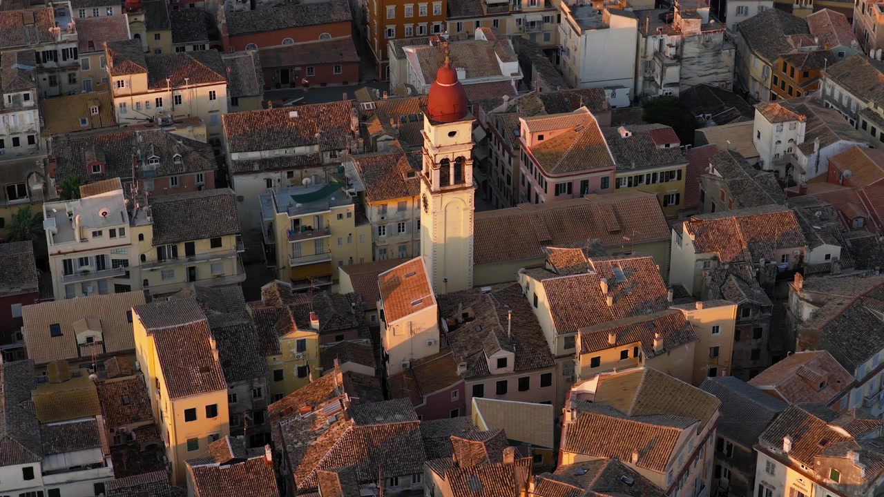 Città Vecchia di Corfù all'alba con densi edifici storici, la torre della Chiesa di San Spiridione e una calda luce dorata