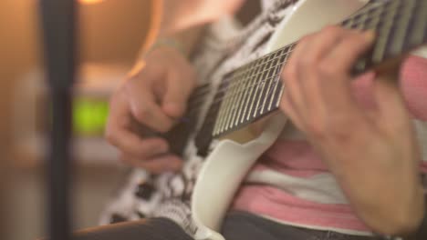 Close-up-of-a-professional-musician-playing-notes-on-an-electric-guitar-with-a-guitar-pick-during-a-live-session-with-warm-studio-lights-and-an-amplifier-in-the-blurred-background