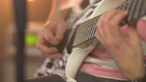 cierre de un músico profesional tocando notas en una guitarra eléctrica con una púa de guitarra durante una sesión en vivo con cálidas luces de estudio y un amplificador en el fondo borroso