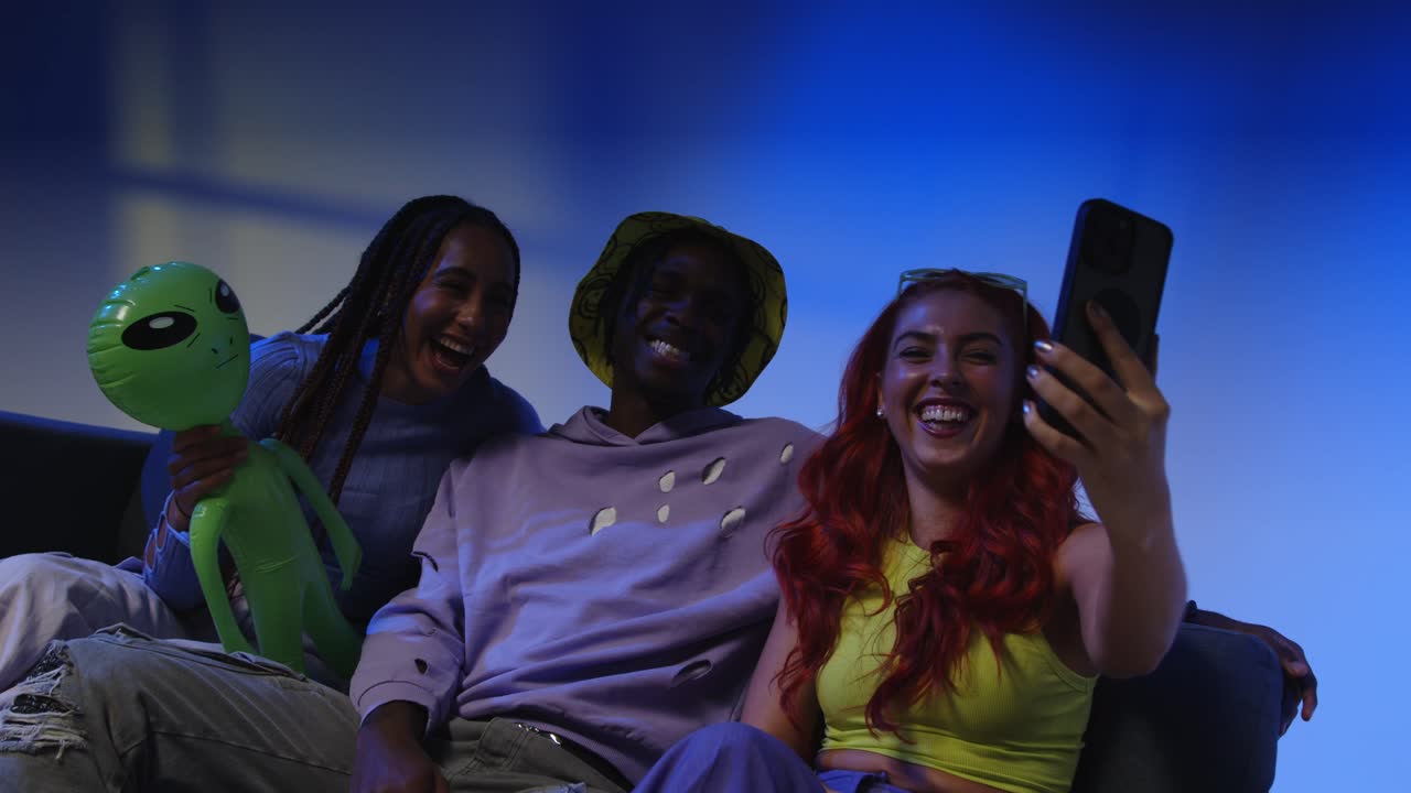 fotografía de estudio de un grupo de amigos de la generación z sentados en el sofá posando para una selfie en un teléfono móvil por la noche con una luz intermitente