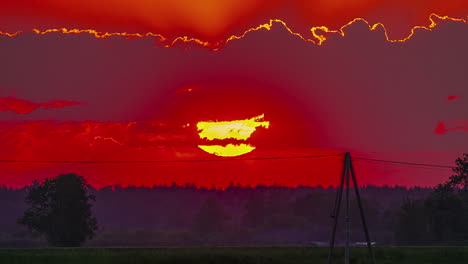 cielo de hora dorada roja de fuego con el sol poniéndose detrás de las nubes sobre el paisaje rural