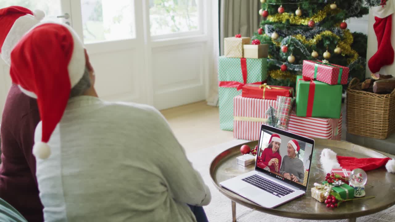 amigas mayores diversas usando una computadora portátil para una videollamada de navidad con una familia sonriente en la pantalla