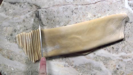 overhead view of hands cutting folded pasta dough into noodles with knife