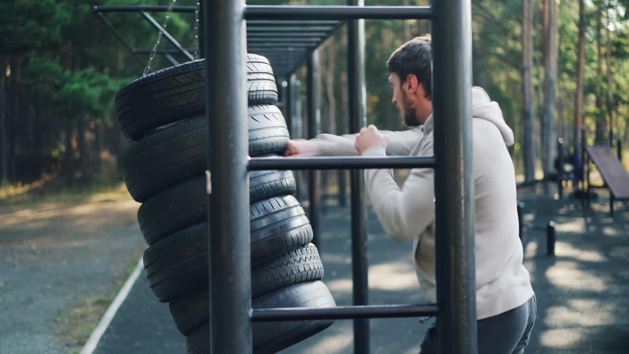 Man working out at an outdoor fitness park using tire punching bag