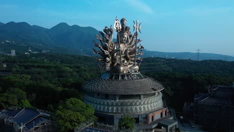 aerial flight towards guanyin goddess silver temple statue against mountain landscape and blue sky in backdrop