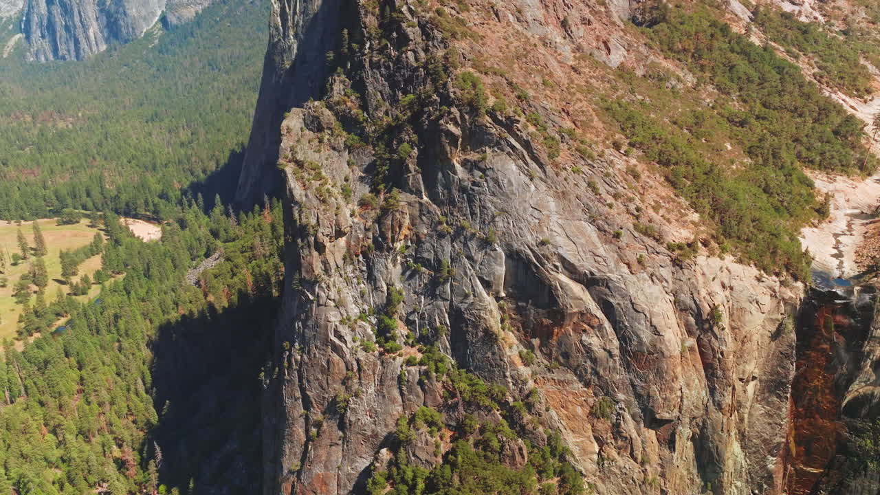 Stunning view of cliff rock at sunny daytime. Little stream flowing from the mountain beside. Lots of pine trees growing at the foot of mountains. Aerial view.