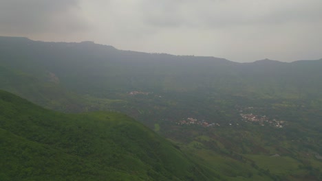 a drone shot captures the lush green mountains of panchgani, maharashtra, draped in monsoon mist, with glimpses of the hill city nestled among the clouds, creating a serene and dreamy landscape