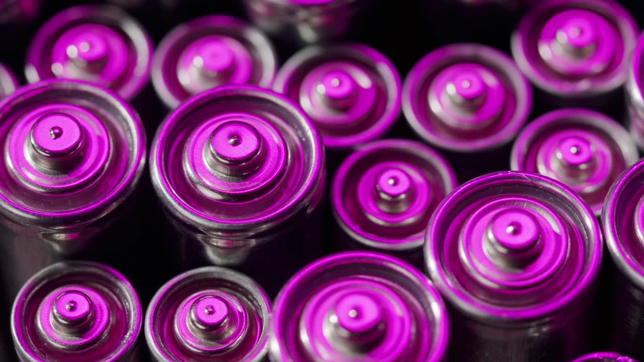 Silver batteries AA and AAA in neon light close-up. Double-A battery is a standard size single cell cylindrical dry battery. Batteries are common in portable electronic devices. An AA battery is composed of a single electrochemical cell that may be either a primary battery or a rechargeable battery.