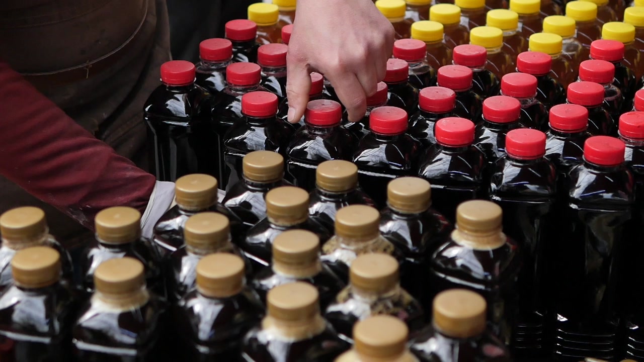 Hands Arranging Rows of Dark Liquid Bottles with Red and Gold Caps