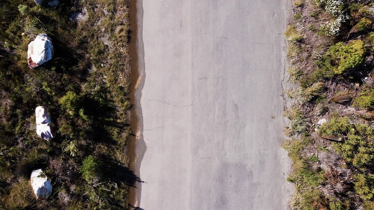 Ciclista MTB in sella con un'ombra perfetta a 90 gradi proiettata dal sole, ripresa aerea dall'alto.