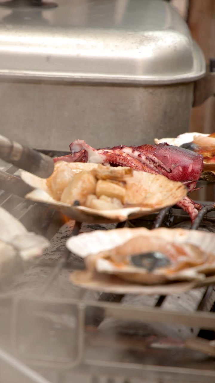 A street vendor uses a blowtorch to sear fresh scallops and seafood on a grill