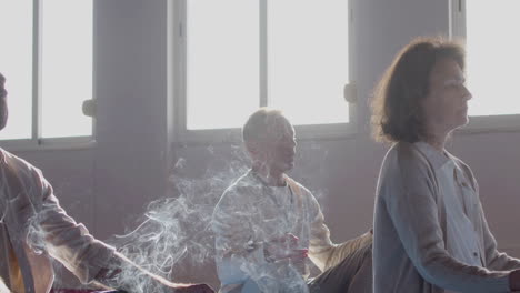 people meditating in yoga studio with smoke from incense sticks