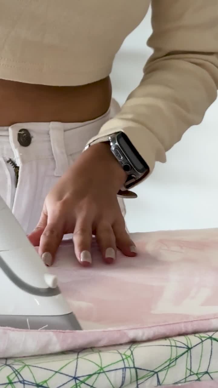 A woman's hands use a steam iron to press pink clothing on an ironing board