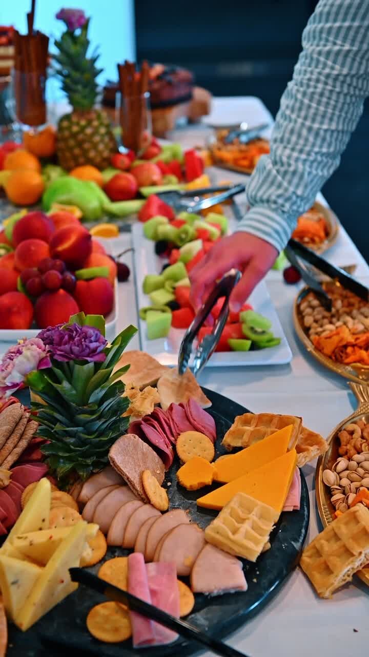 Charcuteribræt og frugtfad på buffetbord. Et udvalg af påskåret kød, oste, kiks, vafler og frisk frugt som ananas og ferskner på et festbord.