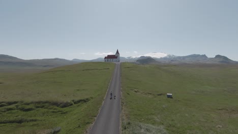 Tourist-with-dog-walking-along-road-from-church-Ingjaldshóll,-icelandic-scenery
