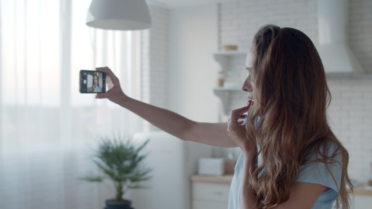 mujer joven tomando una foto selfie en la cocina. mujer guiñando el ojo a la cámara del teléfono.