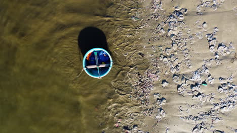 Barco-De-Coracle-Vietnamita-Tradicional-Y-Playa-De-Arena-Llena-De-Plástico-Y-Otra-Suciedad,-Vista-Aérea-De-Arriba-Hacia-Abajo