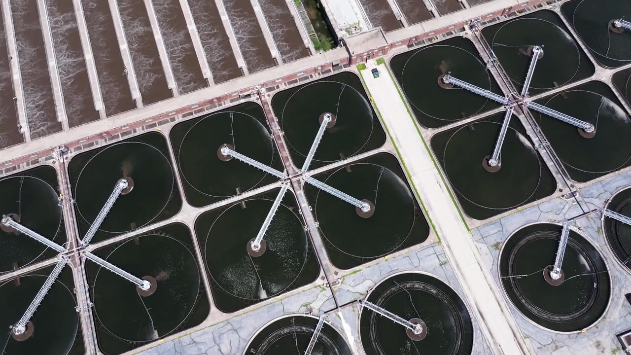 Birds eye drone shot above clarifier tanks and active aeration channels at a water reclamation facility with foam and churning water visible.