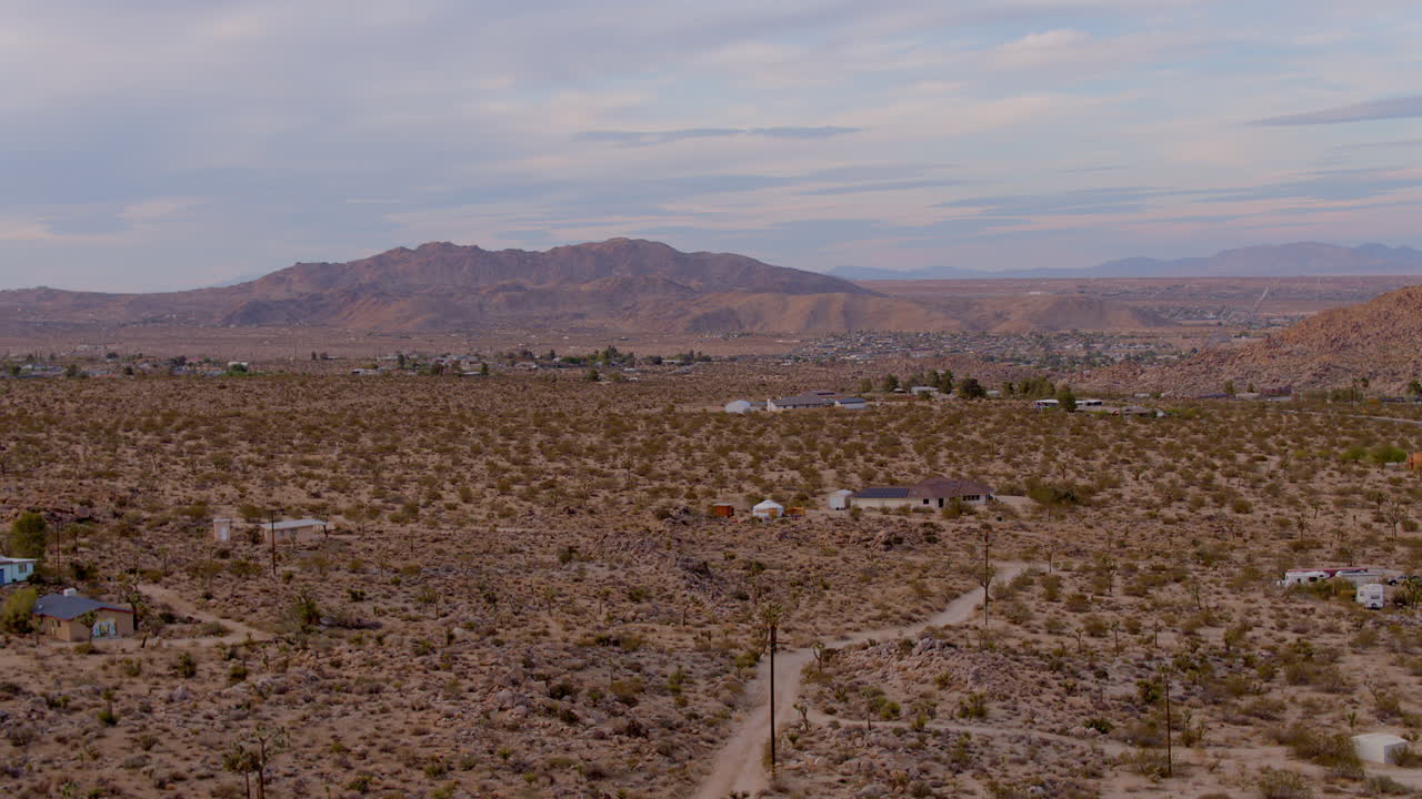 sube por caminos de tierra y casas en el desierto de joshua tree, california, con hermosas montañas en el horizonte