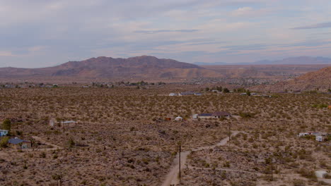 boom up over dirt road and houses in desert of joshua tree, california with gorgeous mountains on horizon