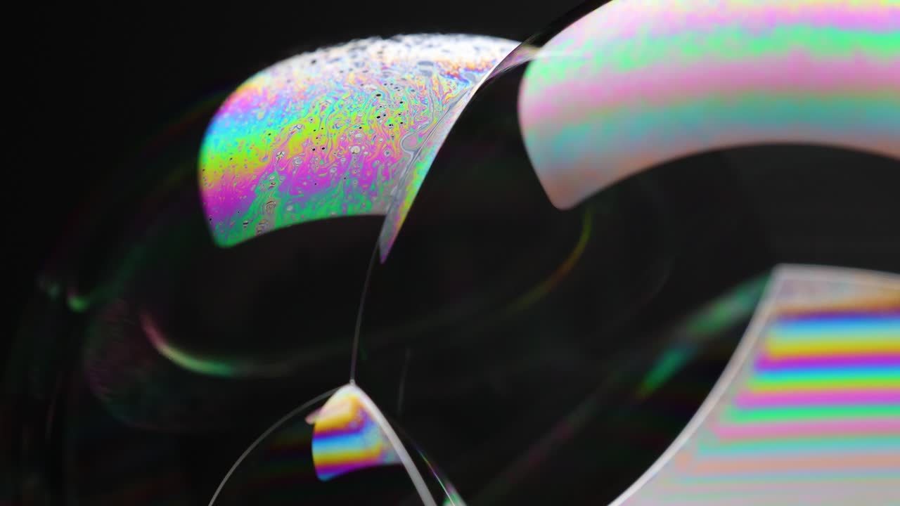 Vibrant soap bubbles display shifting colors and reflections against a dark background, captured in slow motion for a mesmerizing visual effect