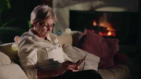 senior woman using smartphone by fireplace