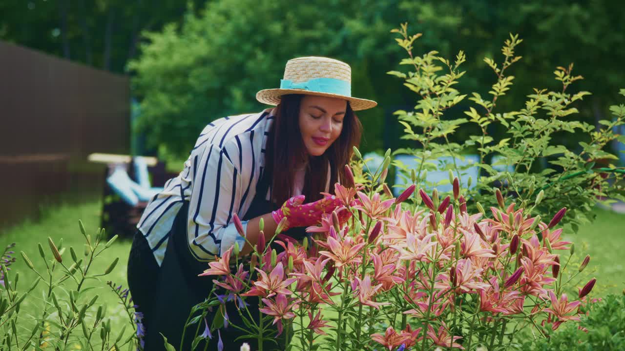 Woman in straw hat enjoying fragrant flowers in a vibrant garden surrounded by greenery