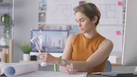 female architect in office working on drawings for renewable energy project with model wind turbine