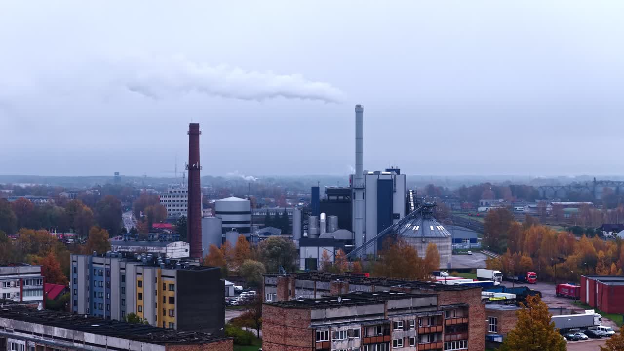 Smoke Billows From Factory Chimneys Amid a Cloudy Industrial Landscape - Aerial Drone Shot
