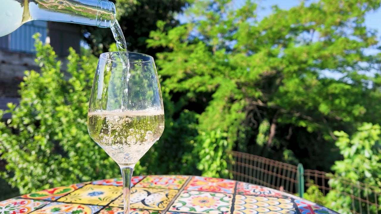 Versamento di vino bianco al rallentatore in un bicchiere su un tavolo a mosaico colorato all'aperto