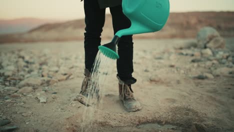 refugee person mindlessly watering an arid sandy soil in the desert at dawn