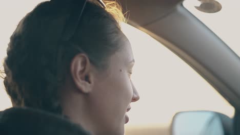 밝은 저녁 태양은 차에 앉아있는 즐거운 여인에게 빛납니다.