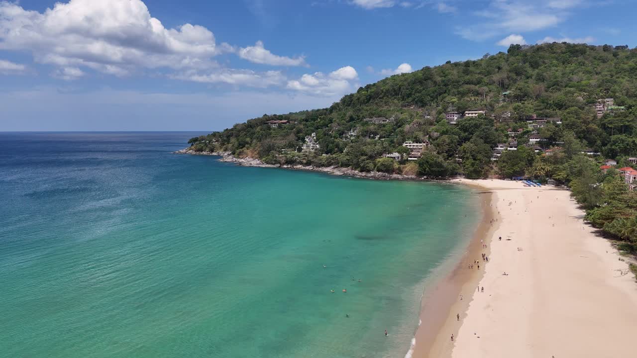 드론 촬영은 태국 푸켓의 조용한 해변을 포착합니다. 은 하늘 아래 푸른 물, 모래 해변, 울창한 초록색을 보여줍니다.
