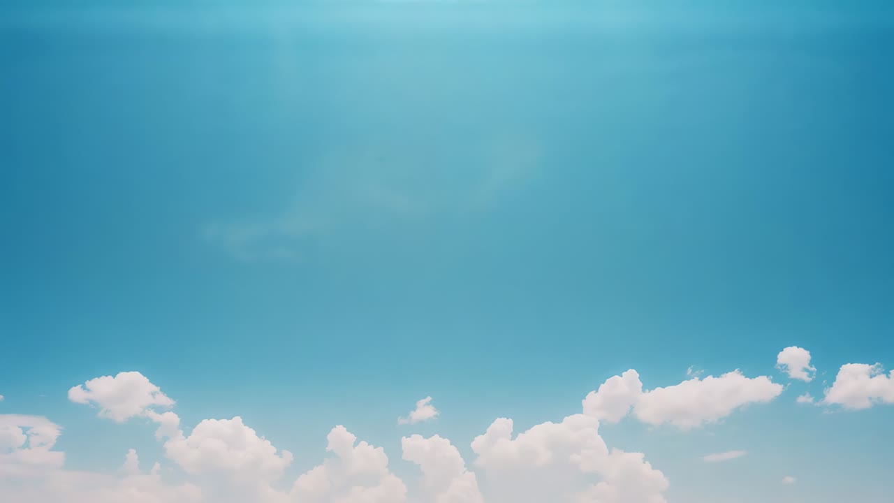 Drifting white cumulus cloud bank crossing blue sky, being carried by light breeze with lens flare