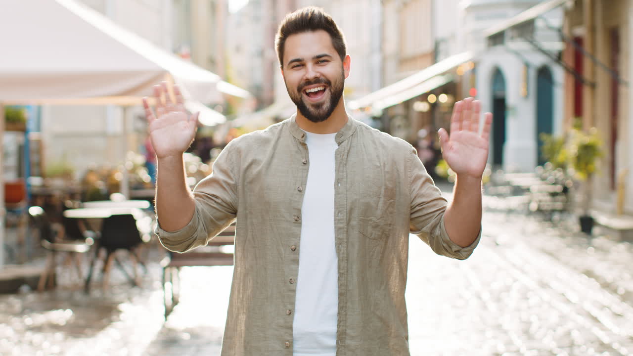 joven sonriendo amistosamente a la cámara agitando las manos hola hola saludo o adiós en la calle de la ciudad