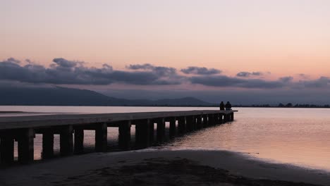 anonymous persons sitting on pier near sea at sunset