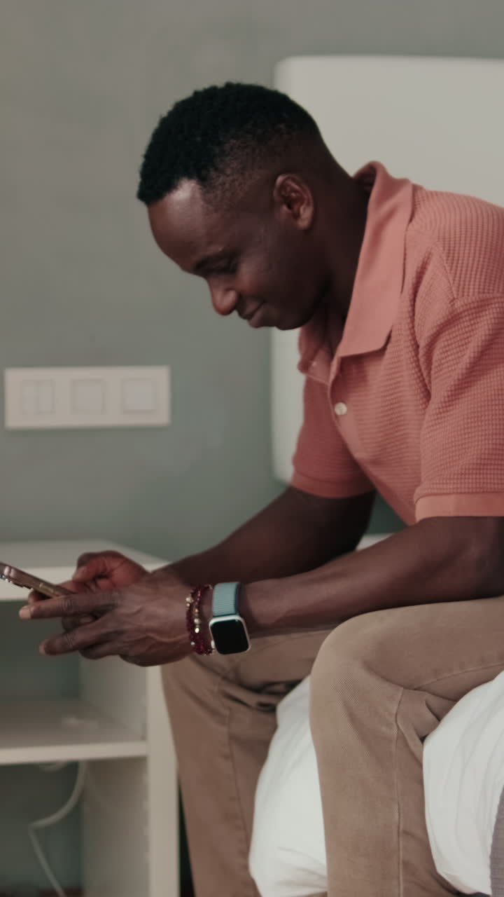 African American Man Sitting on Bed and Using Smartphone
