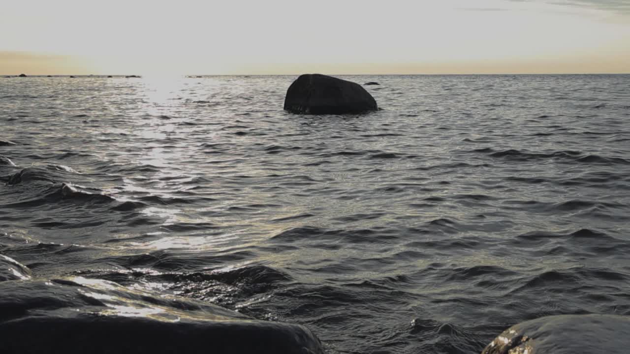 서루피 에스토니아 해변에서 저녁과 저녁 시간 동안 물에 있는 바위와 함께 해안을 때리는, 가라앉는 태양을 반사하는 파도의 느린 동작 영상.