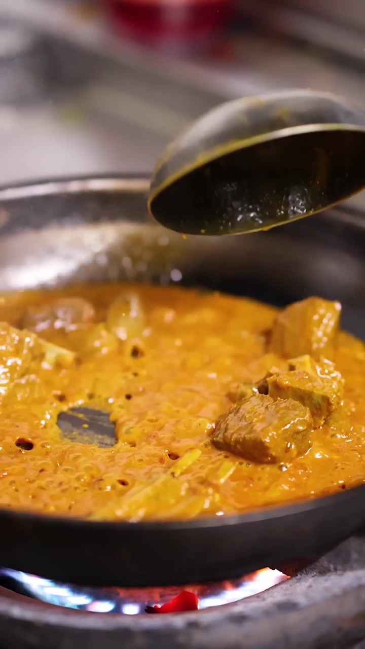 Primo piano di curry arancione che sobbolle in una padella su una fiamma a gas con un mestolo di metallo