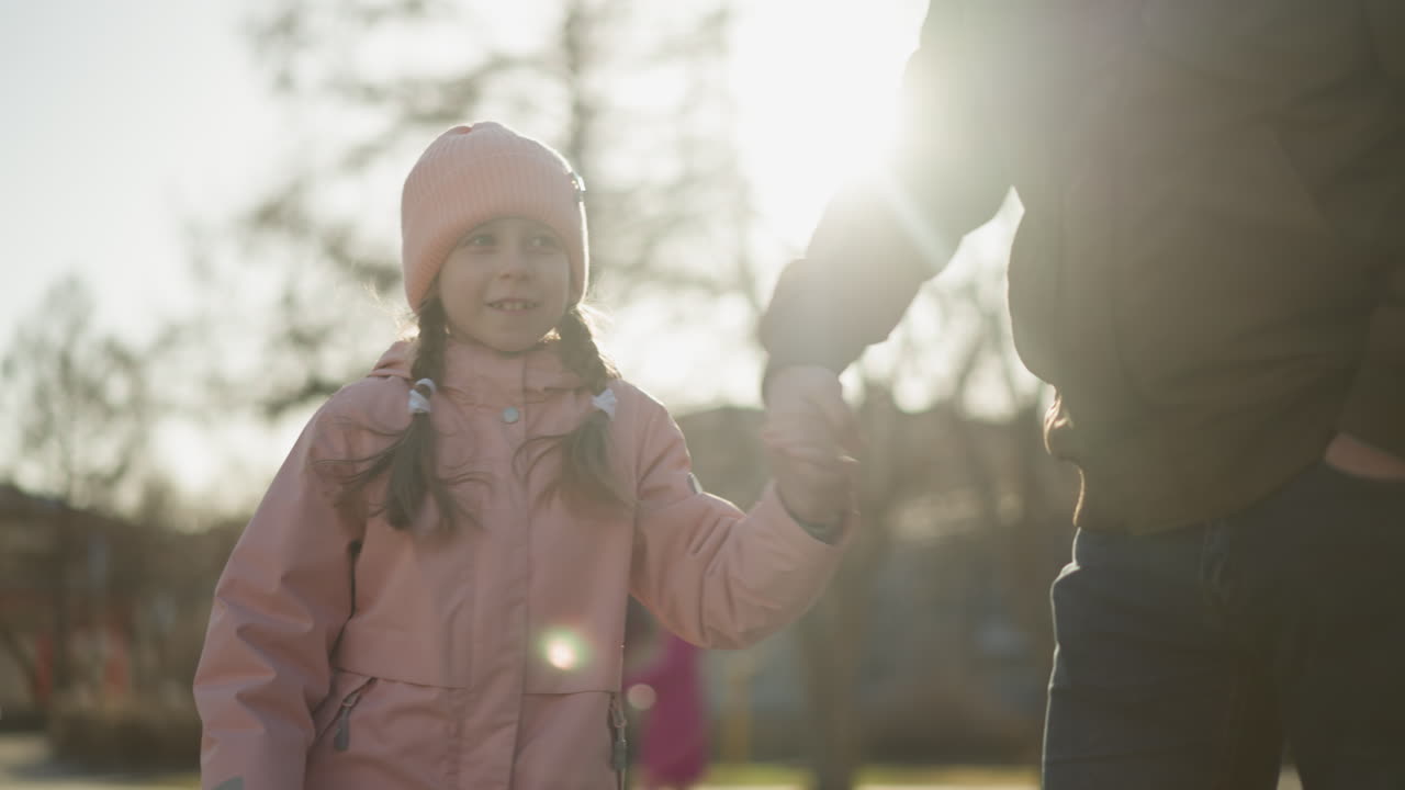 핑크색 모자와 재을 입은 어린 소녀가 갈색 재과 파란 청바지를 입은 얼굴 없는 남자에게 돌아다니고 있습니다. 놀이하는 순간은 공원에서 은 날의 기과 따뜻함을 포착합니다.