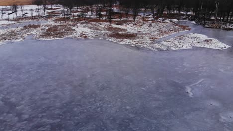 drone over frozen icy winter pond in forest